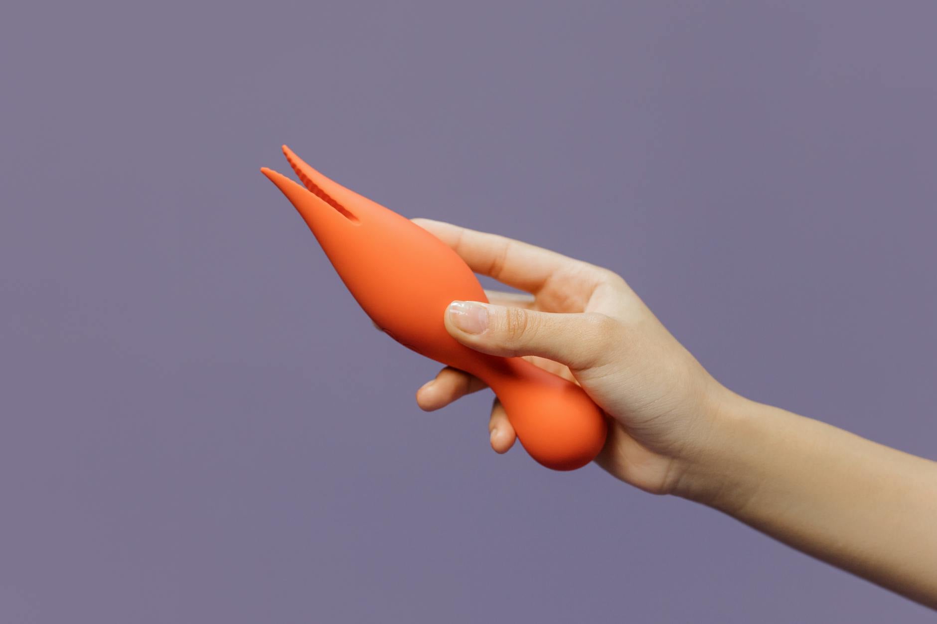 Close-up of a hand holding a vibrator against a minimalistic purple backdrop, showcasing modern intimacy.