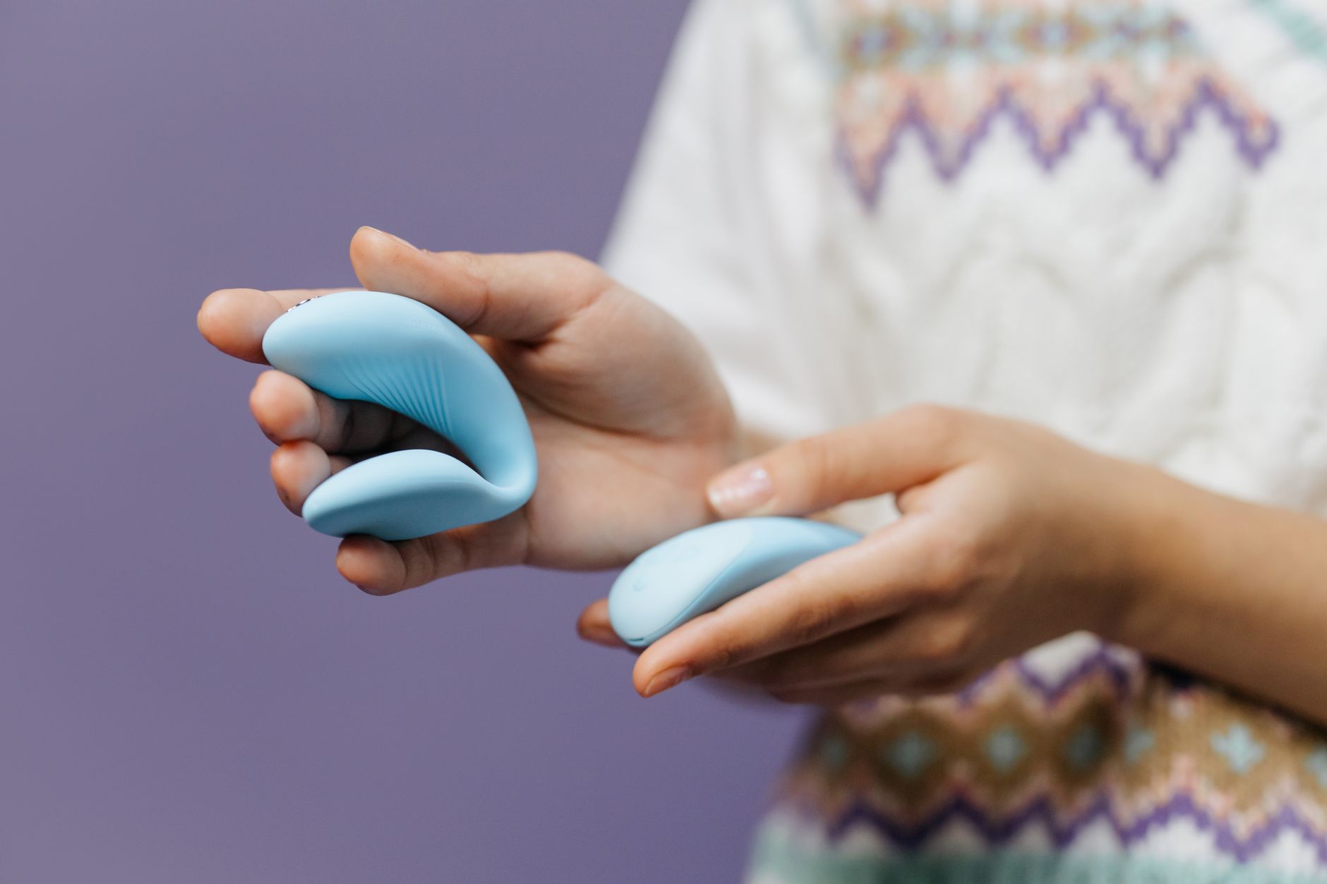 Vibrador azul personal sostenido en mano contra fondo púrpura