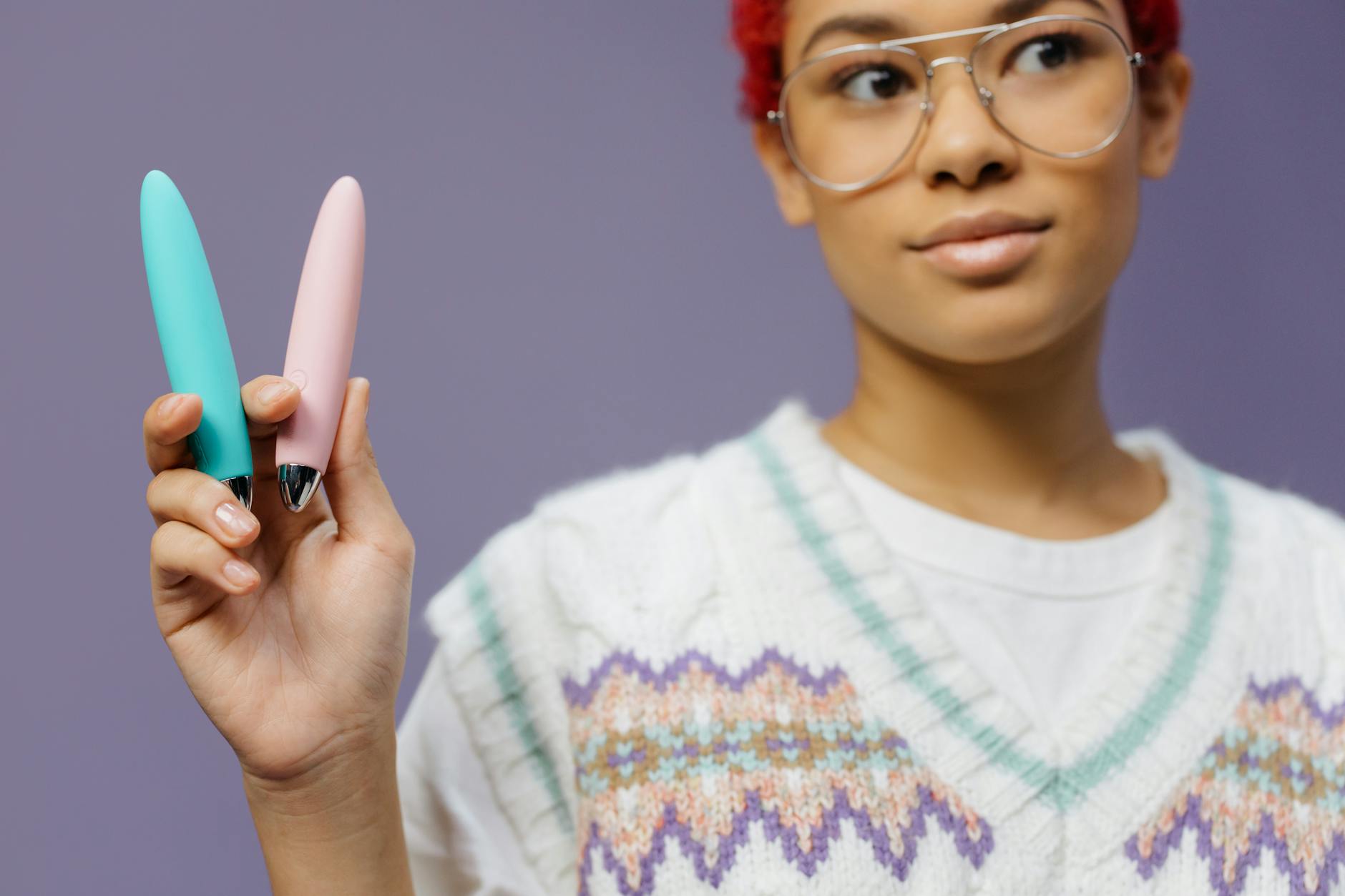 Close-up of hands holding a blue clitoral vibrator against a knitted sweater