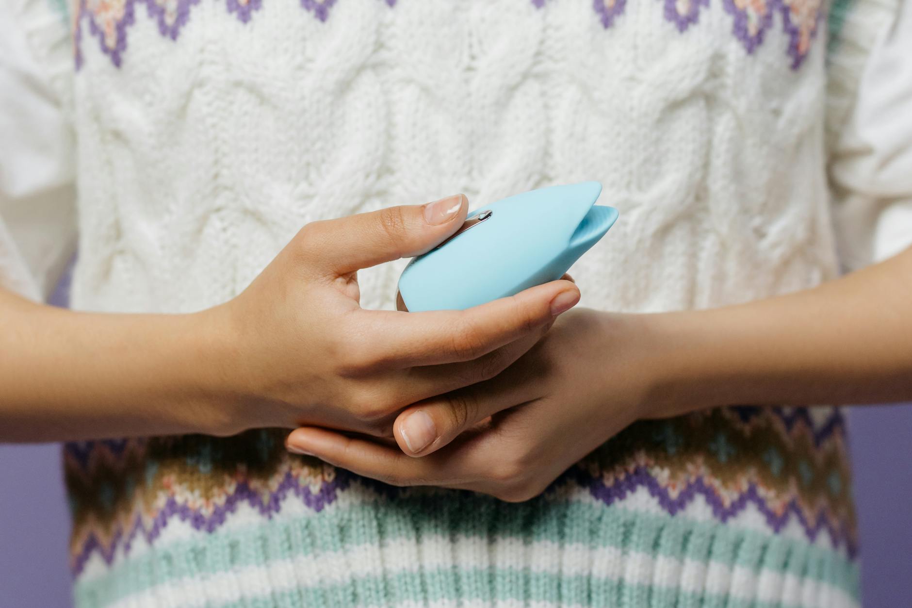 Manos sosteniendo vibrador azul personal contra un fondo de suéter tejido