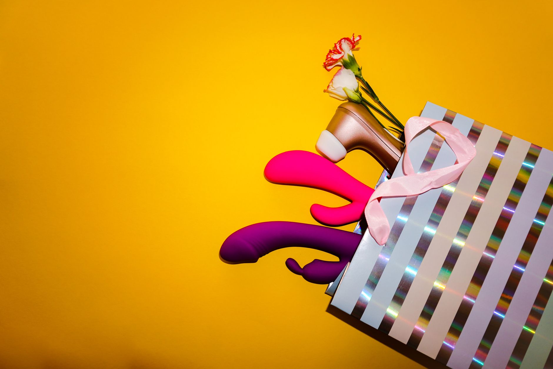 Colorful vibrators with flowers in a holistic gift bag against a bright yellow background