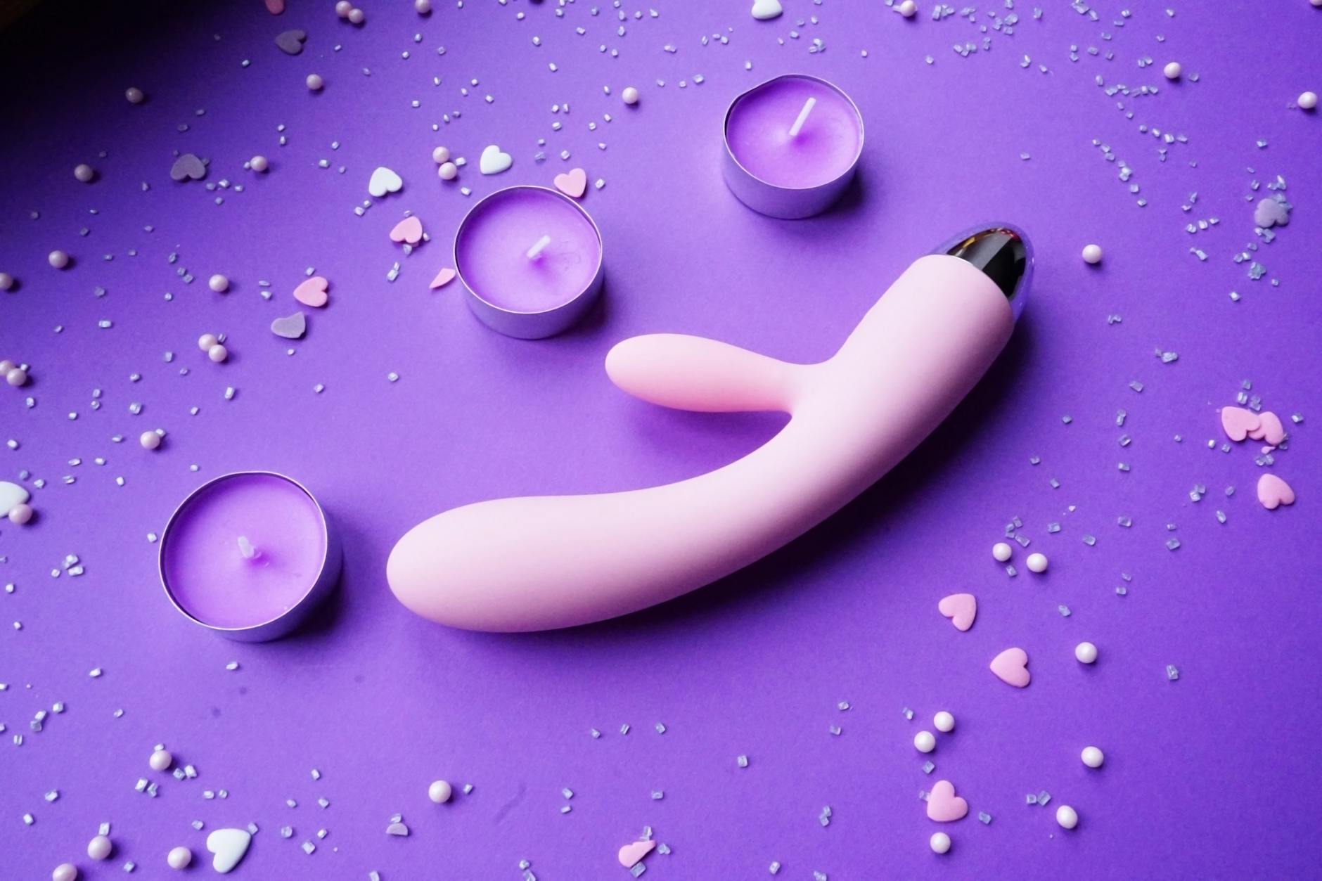 Vibrador rosa vibrante sobre fondo púrpura con confeti de corazones y velas para un ambiente romántico